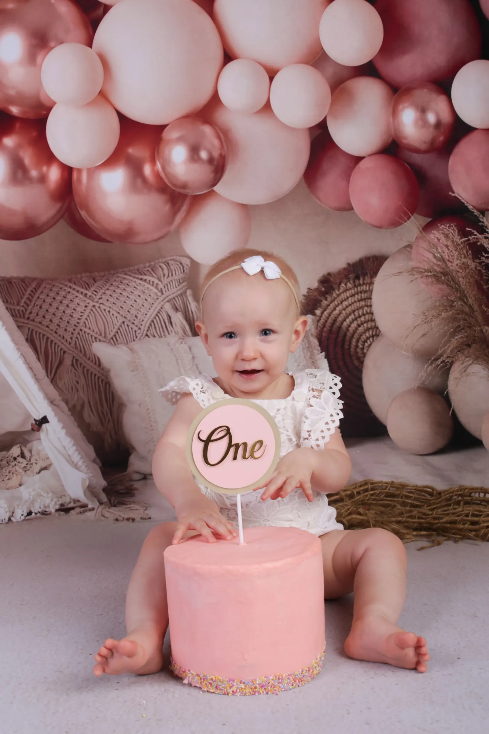 One year old girl with a pink One cake under pink and white balloons