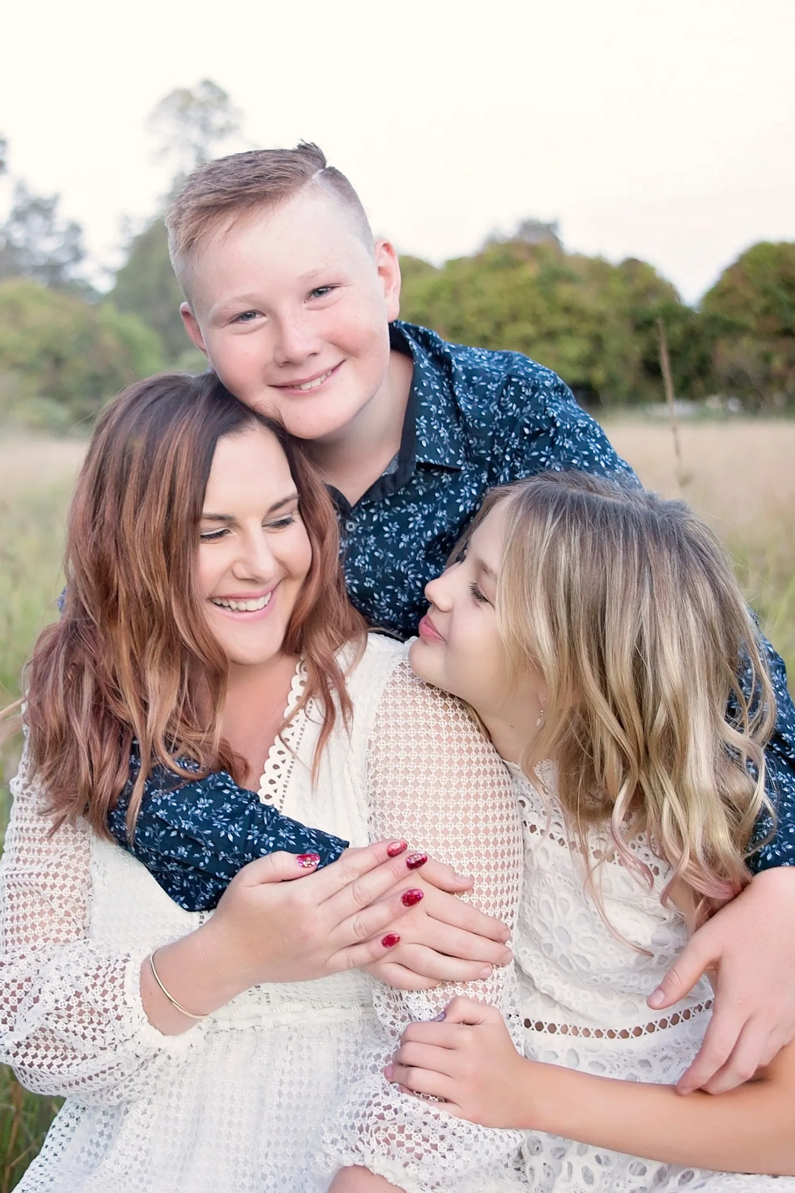 A mum laughing with her son and daughter in a sunlit field