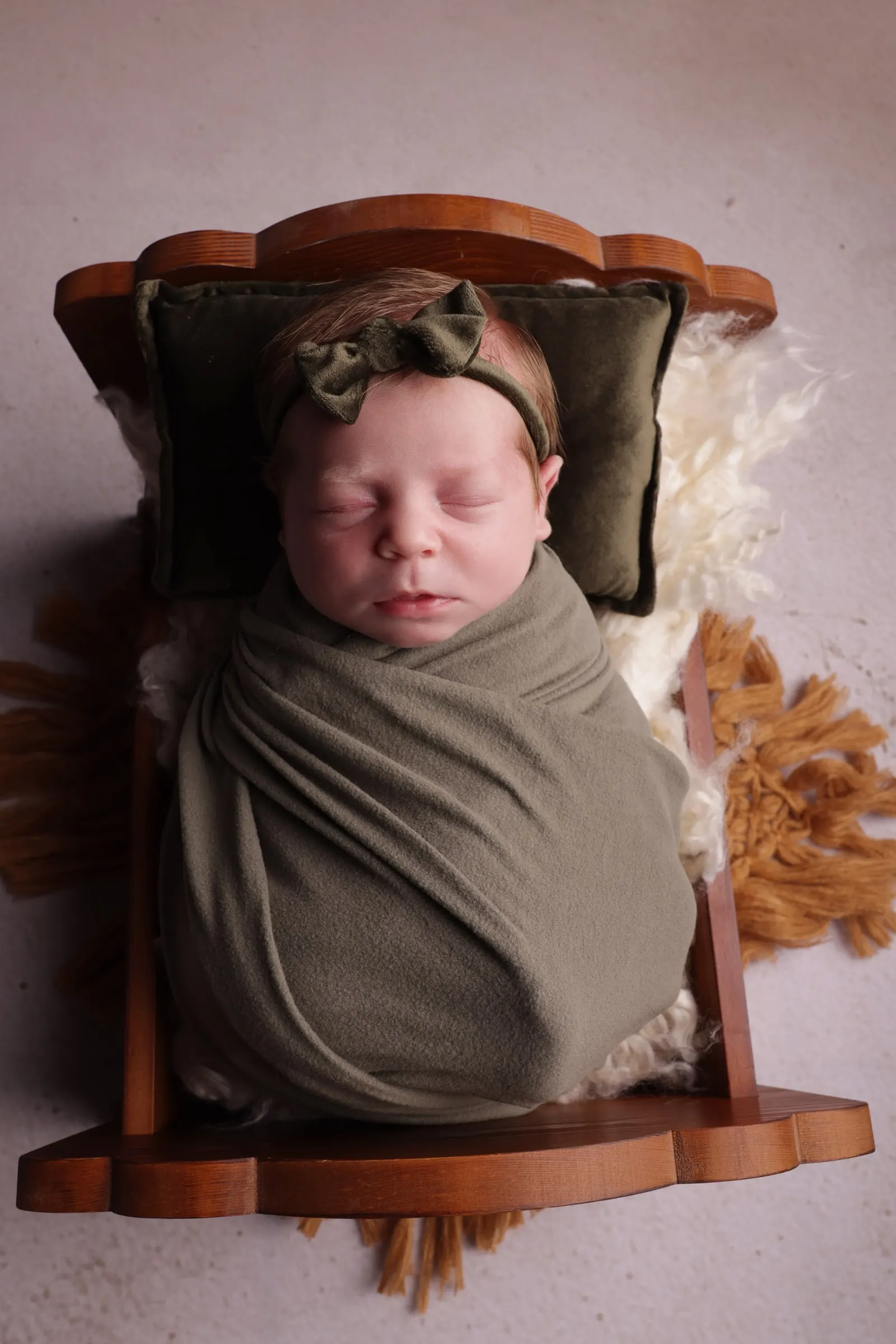 Newborn asleep in a miniature wooden cot, wrapped in olive green