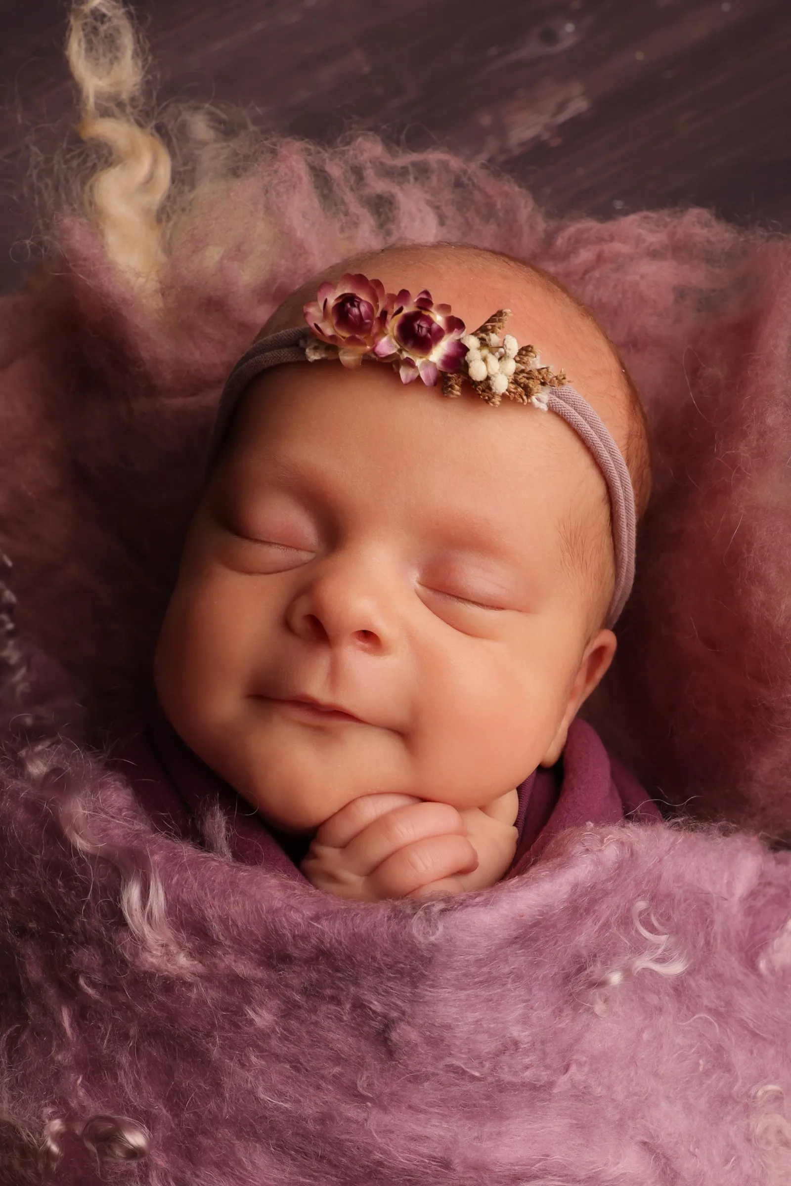 A sleeping newborn smiling in a flower headband