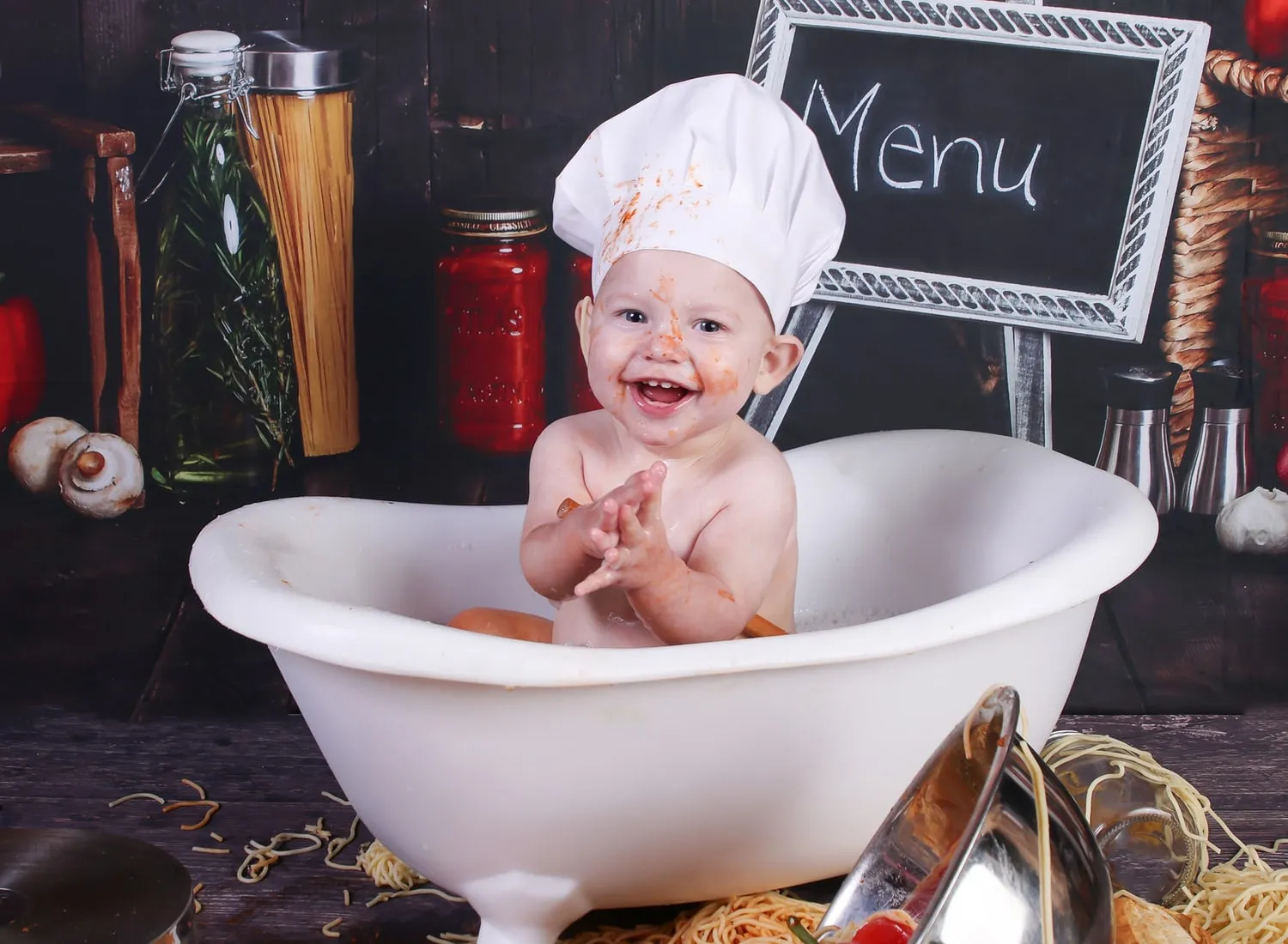 A one year old in a chef hat laughing in a bubble bath