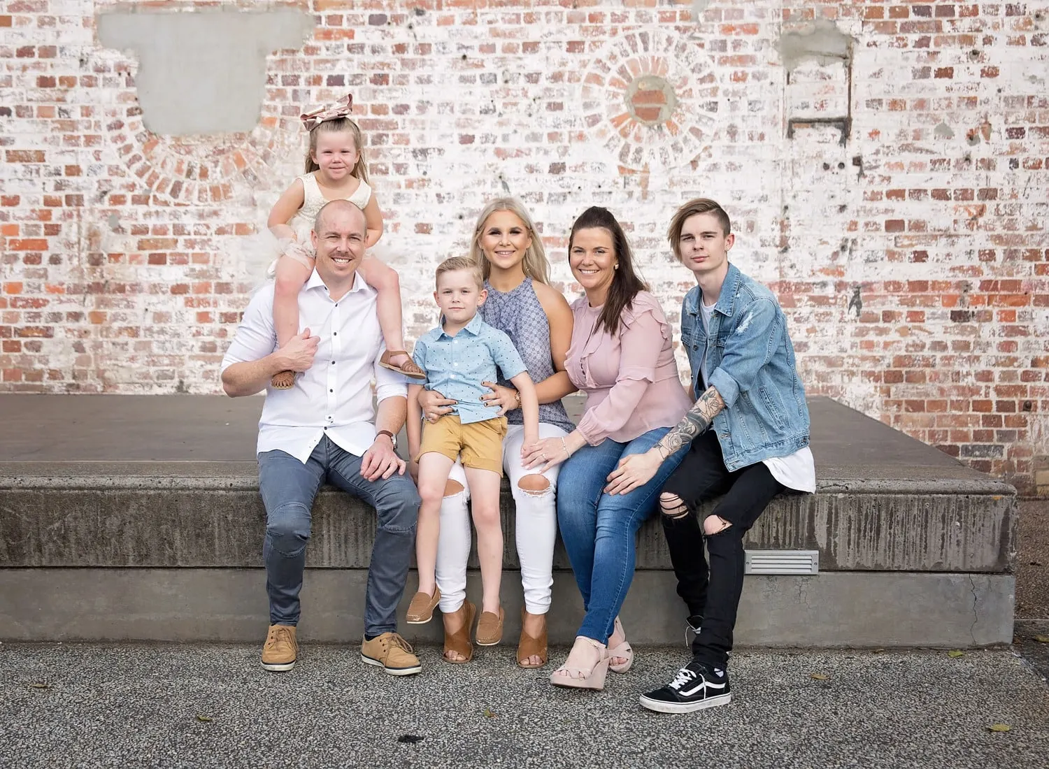Family of six sitting on steps by an old brick wall