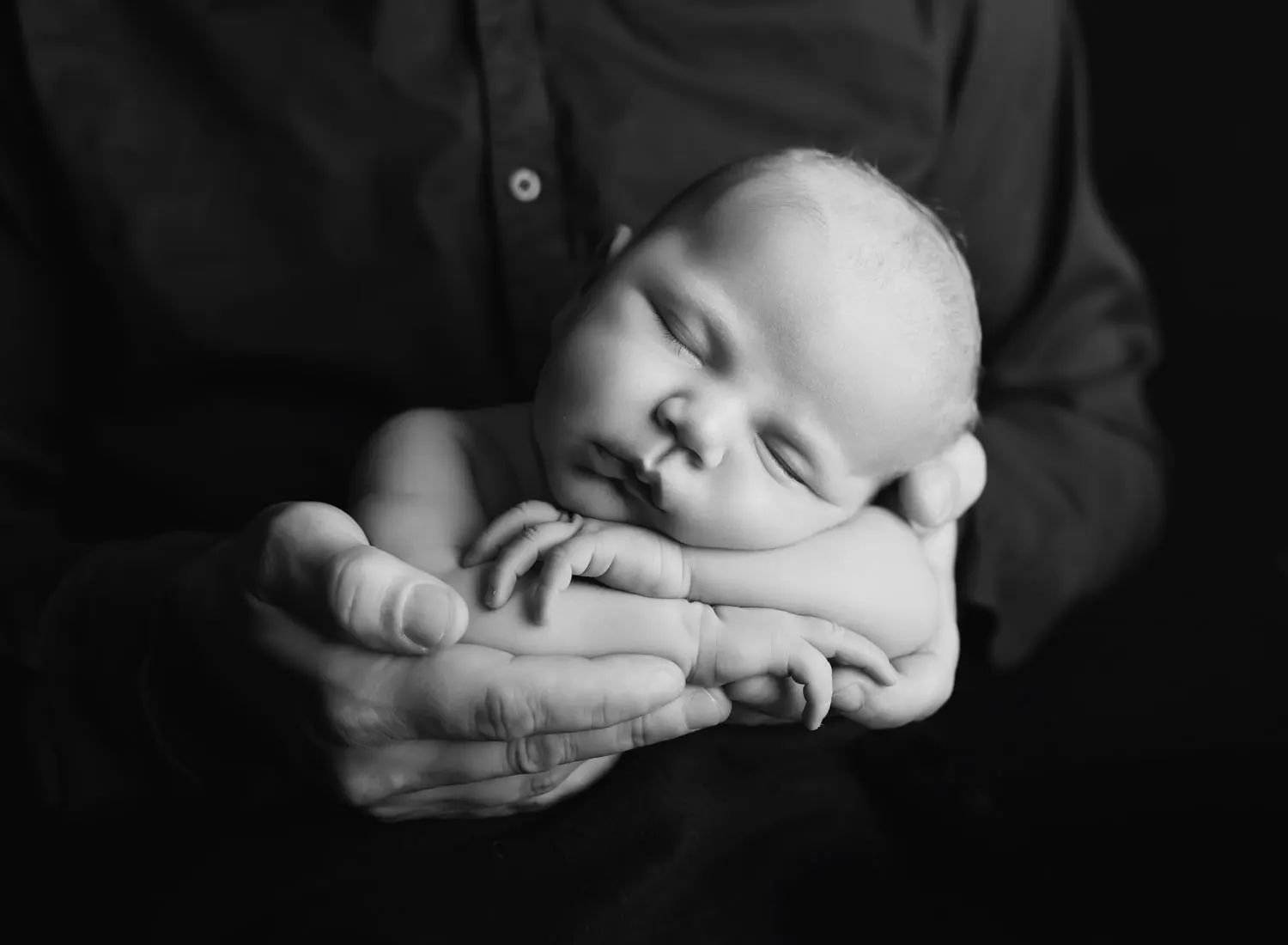 Black and white photo of a newborn asleep in dad's hands