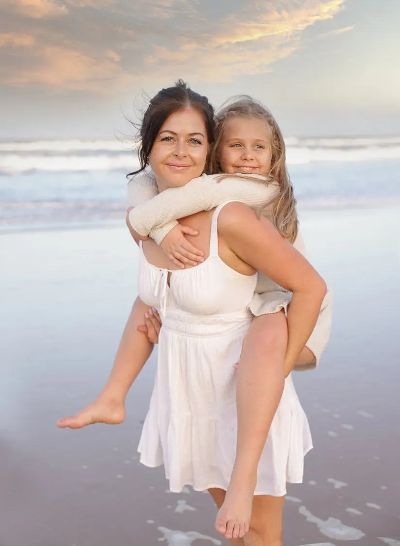 Mum piggybacking her daughter on the beach at sunset
