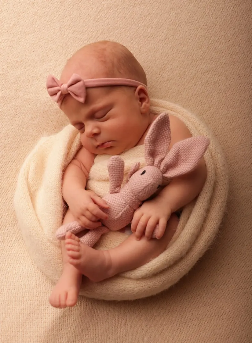 Newborn wrapped in cream cuddling a pink knitted bunny