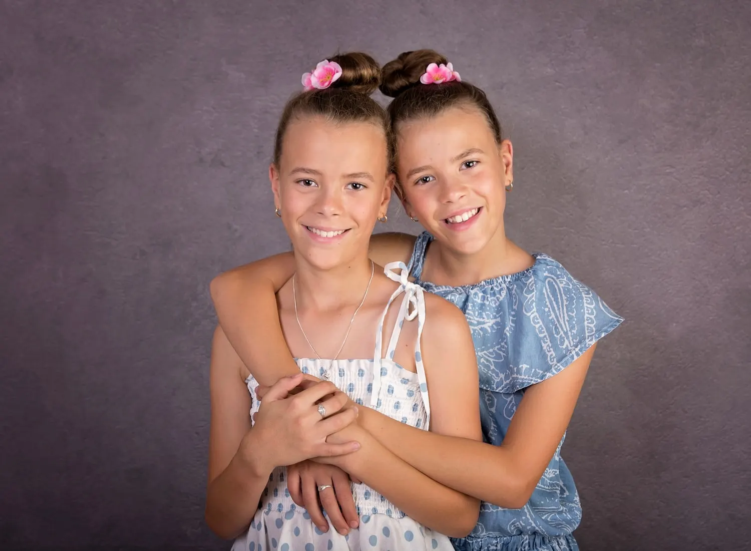 Two sisters hugging in the studio, pink bows in their hair