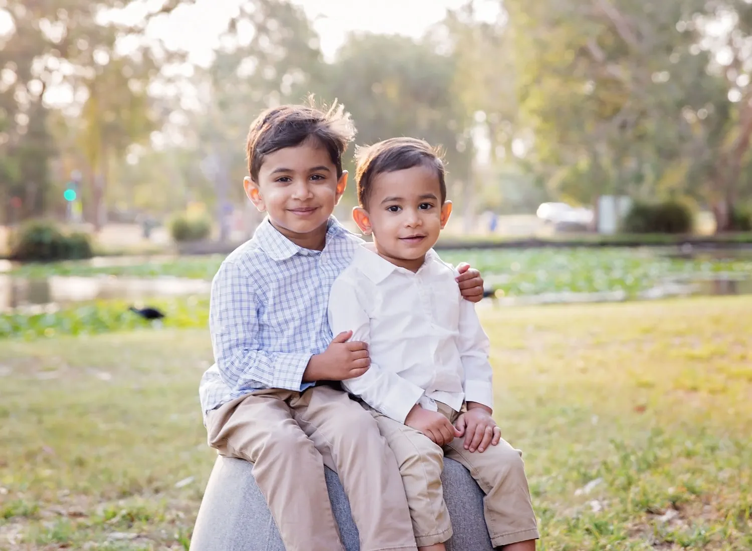 Two brothers in white shirts sitting together in a park