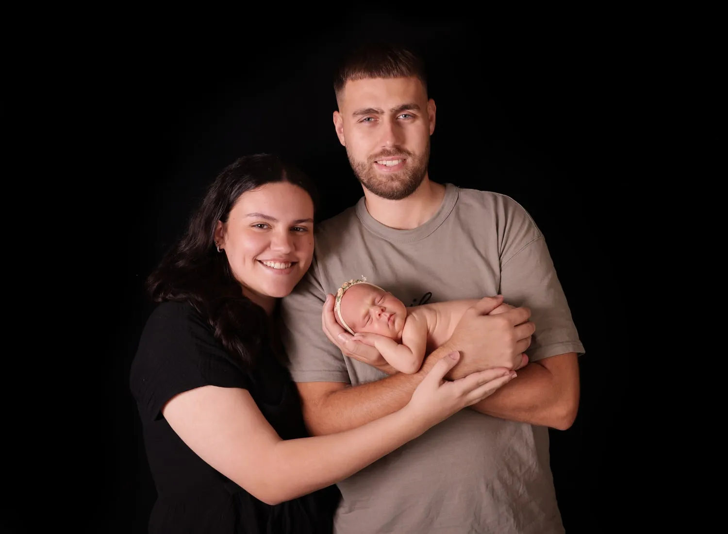 Mum and dad holding their newborn on a black backdrop