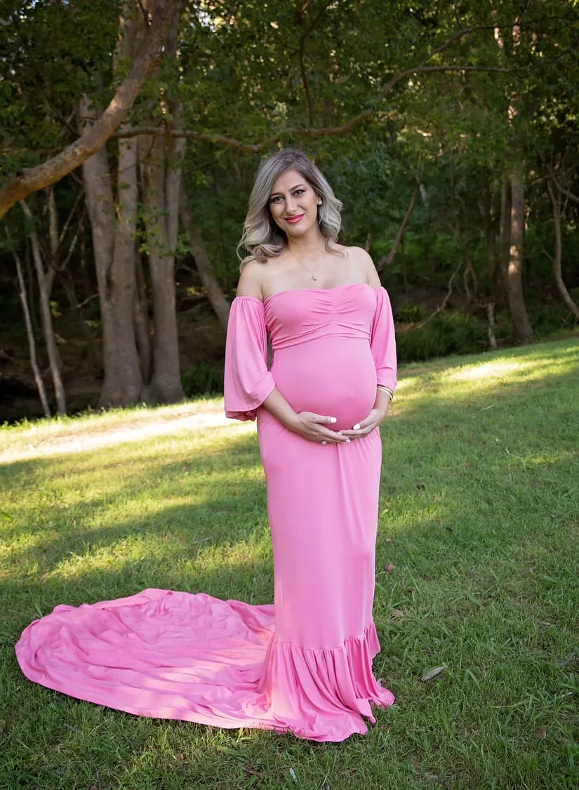 A mum-to-be in a long pink gown in a park