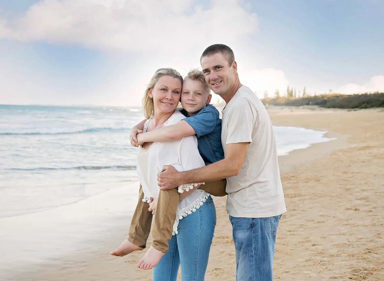 Mum, dad and son hugging on the beach