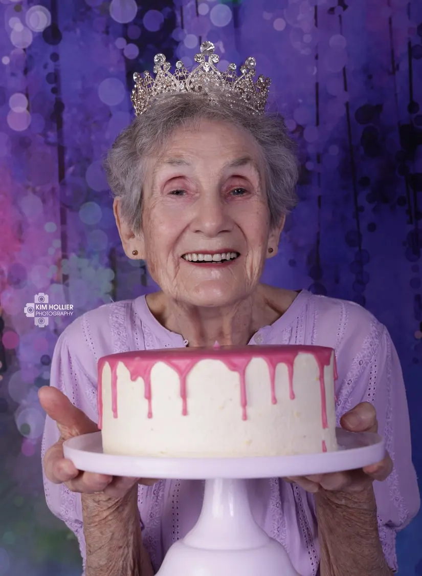 Birthday girl turning 92, in a tiara, holding a pink drip cake