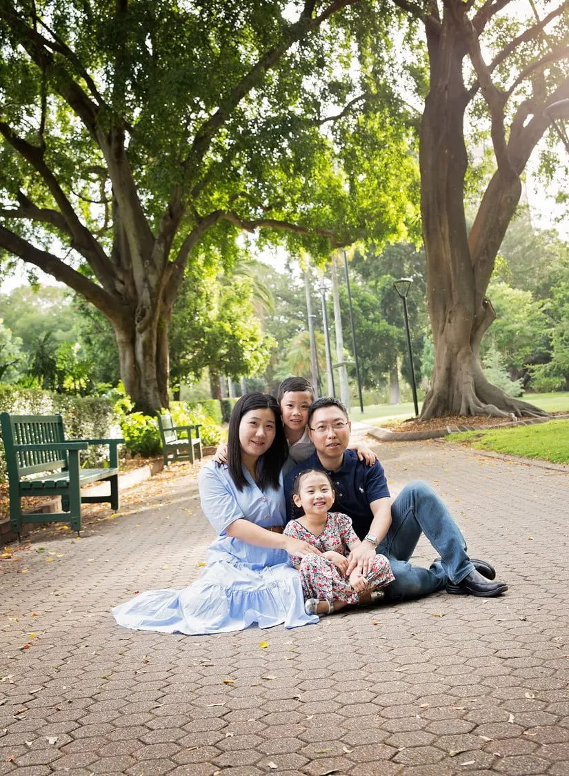 Family of three on a paved path under big fig trees