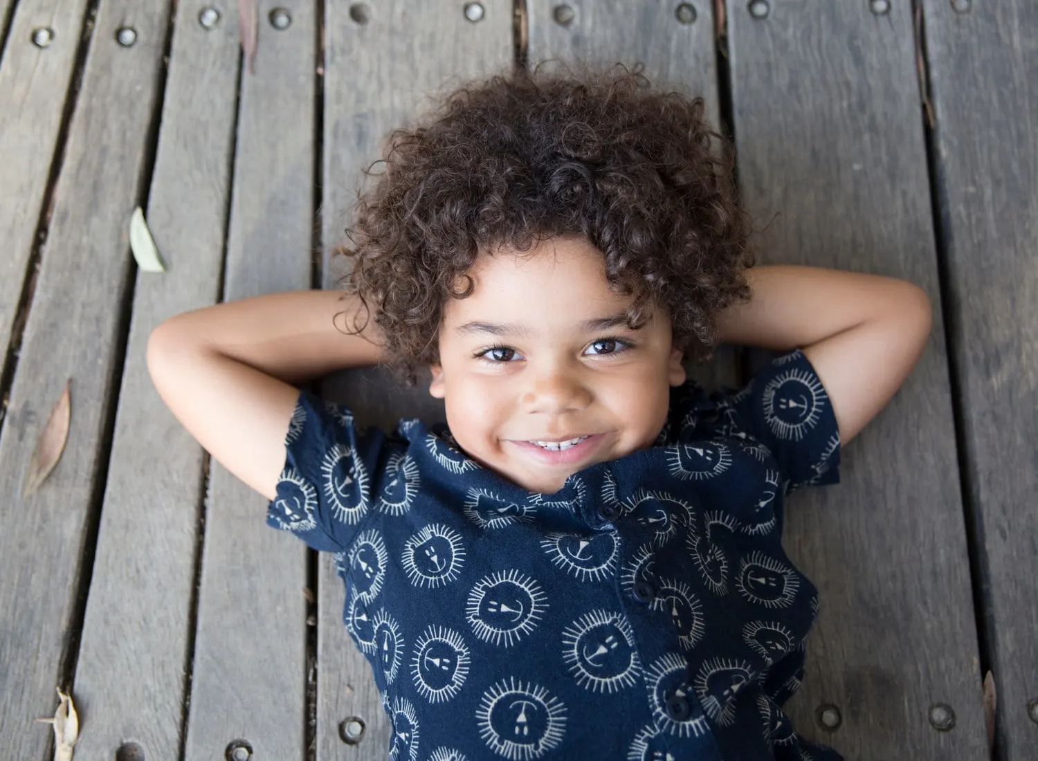 Curly haired boy lying on a timber deck, smiling