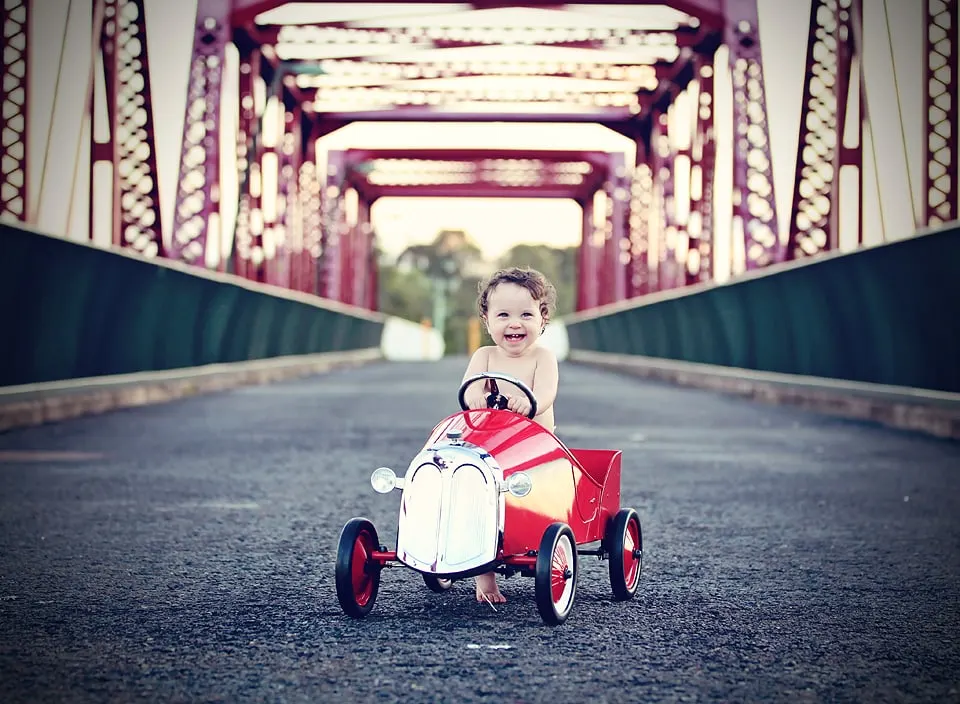 Toddler in a red pedal car on an old bridge