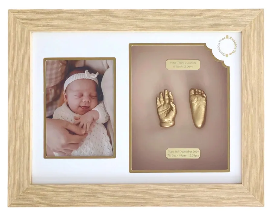 Gold baby hand and foot castings beside a newborn photo, in a light oak frame