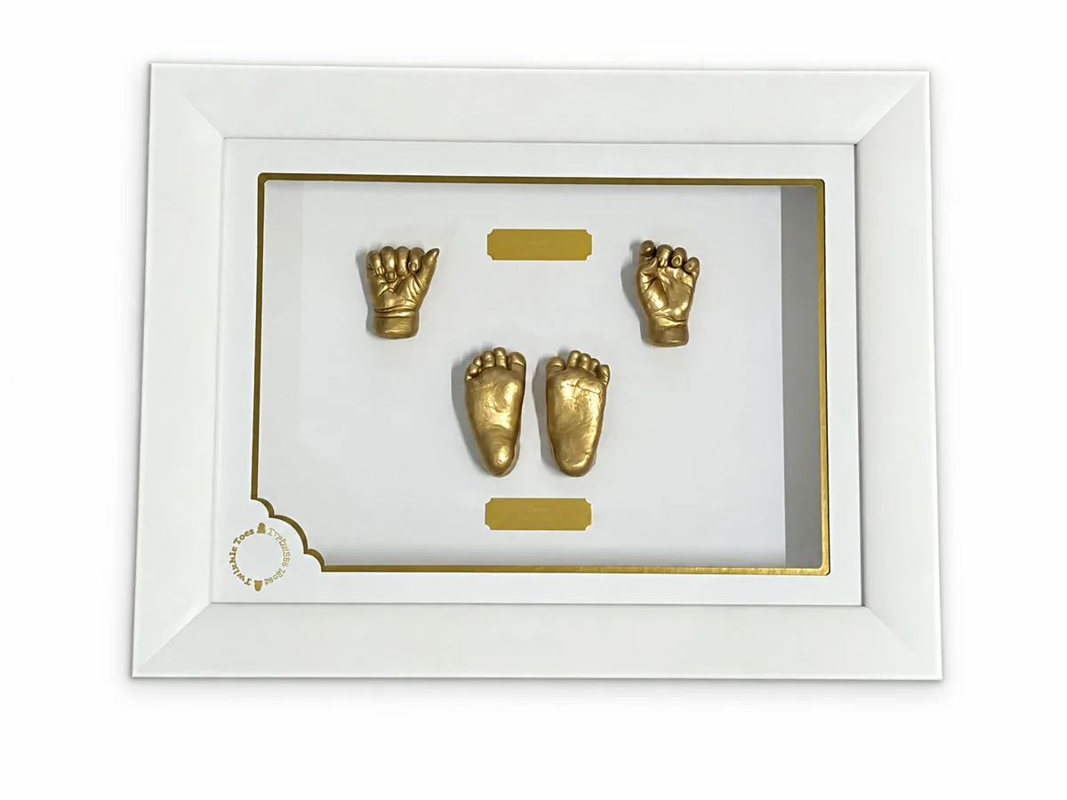 Four gold baby hand and foot castings with engraved plaques, in a white frame